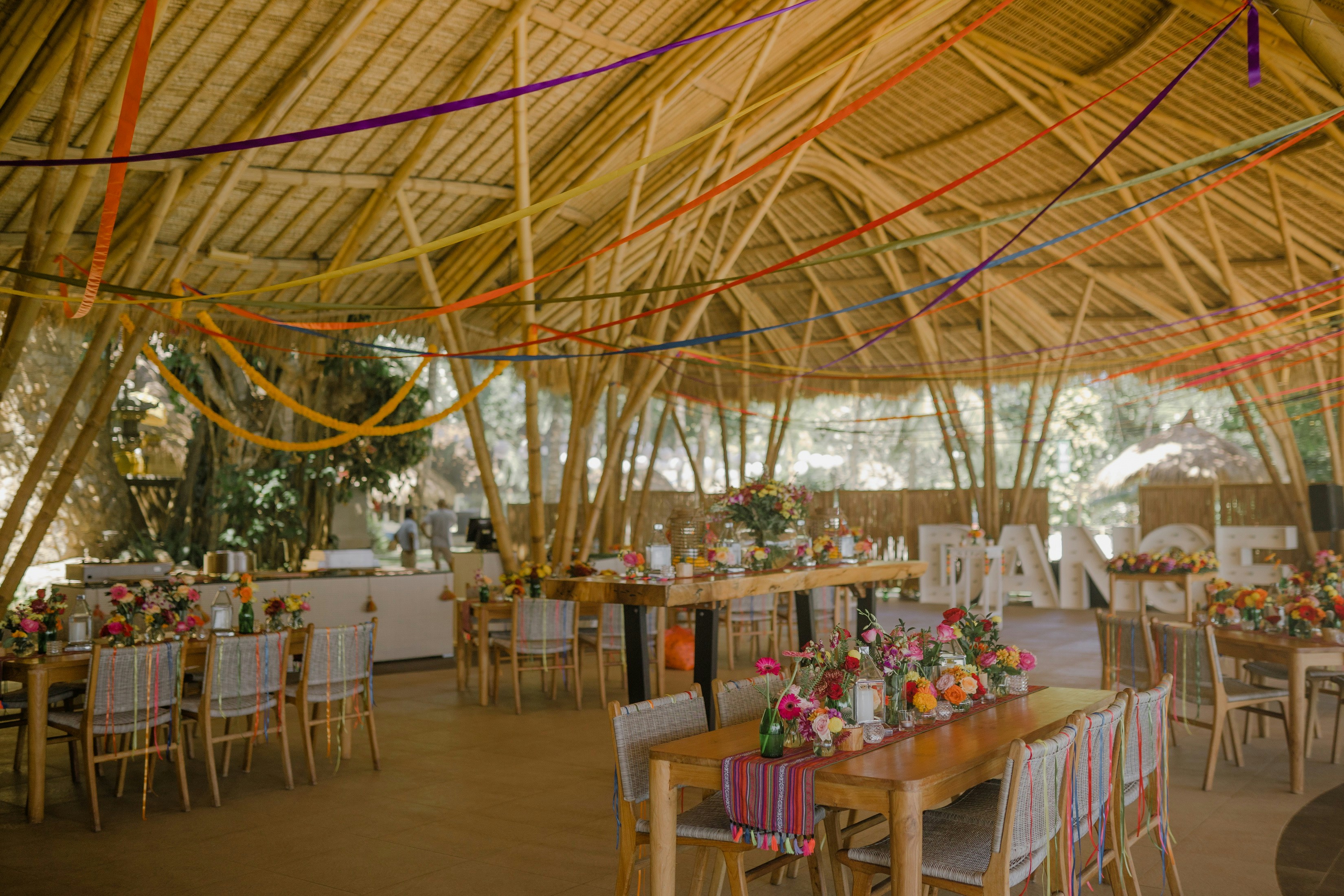 Styled celebration table with white chairs, woven pendant lights, and a floral backdrop